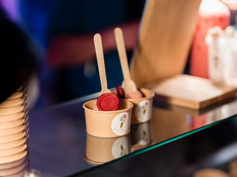 Zwei Becher mit Eis und Sorbet, jeweils mit Holzlöffel, auf einer Theke.
